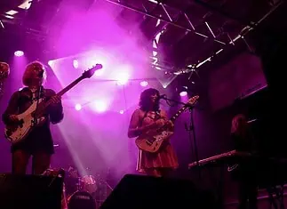 Catch these scene-leading locals opening for can’t-miss nationals across OKC Band performing on a lit stage with purple lights; two guitarists and a keyboard player, drum kit in back, vintage TV on a red pedestal to the left.